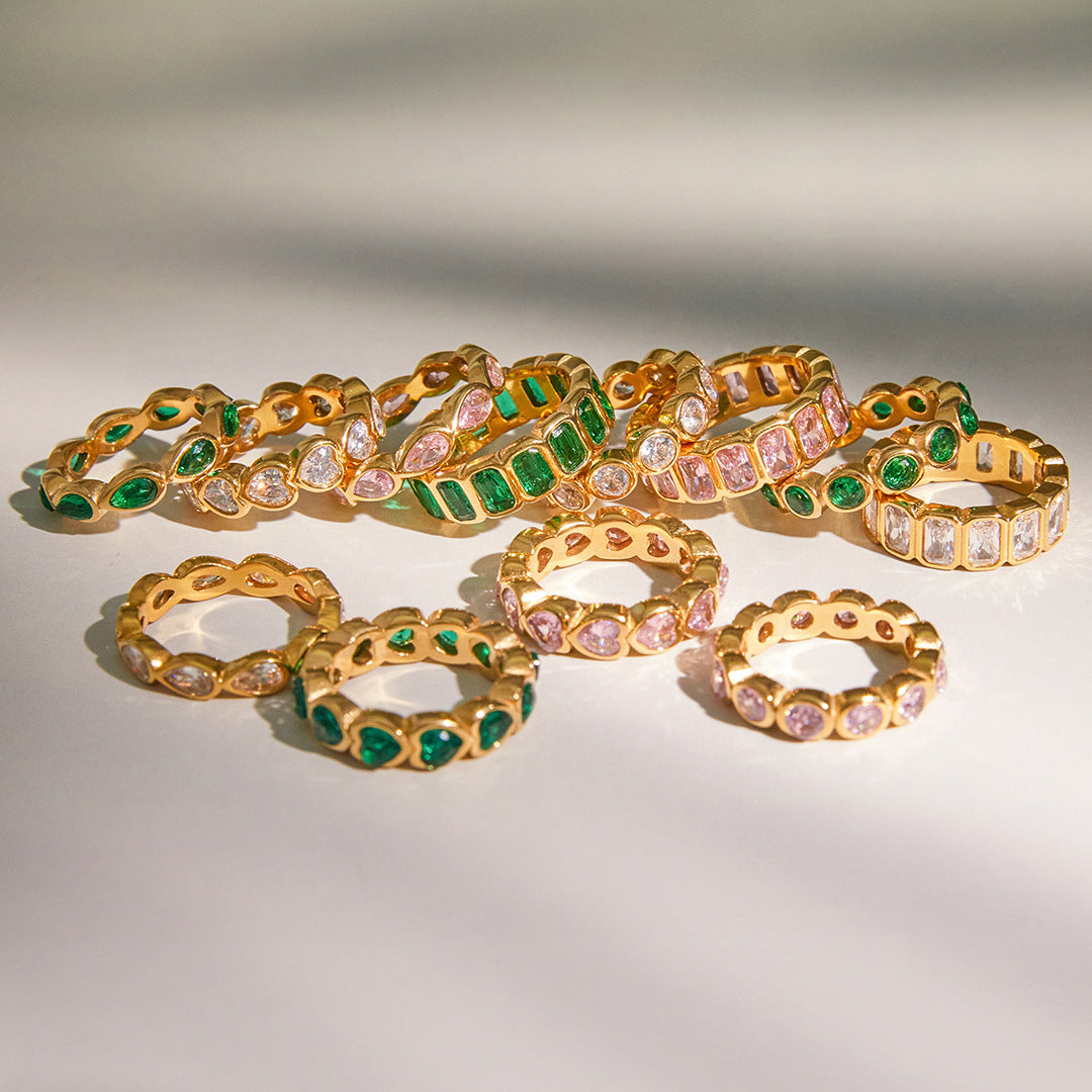 Crystal eternity rings in green, pink and clear laid out on a pale surface