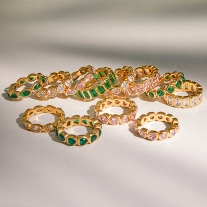 Crystal eternity rings in green, pink and clear laid out on a pale surface