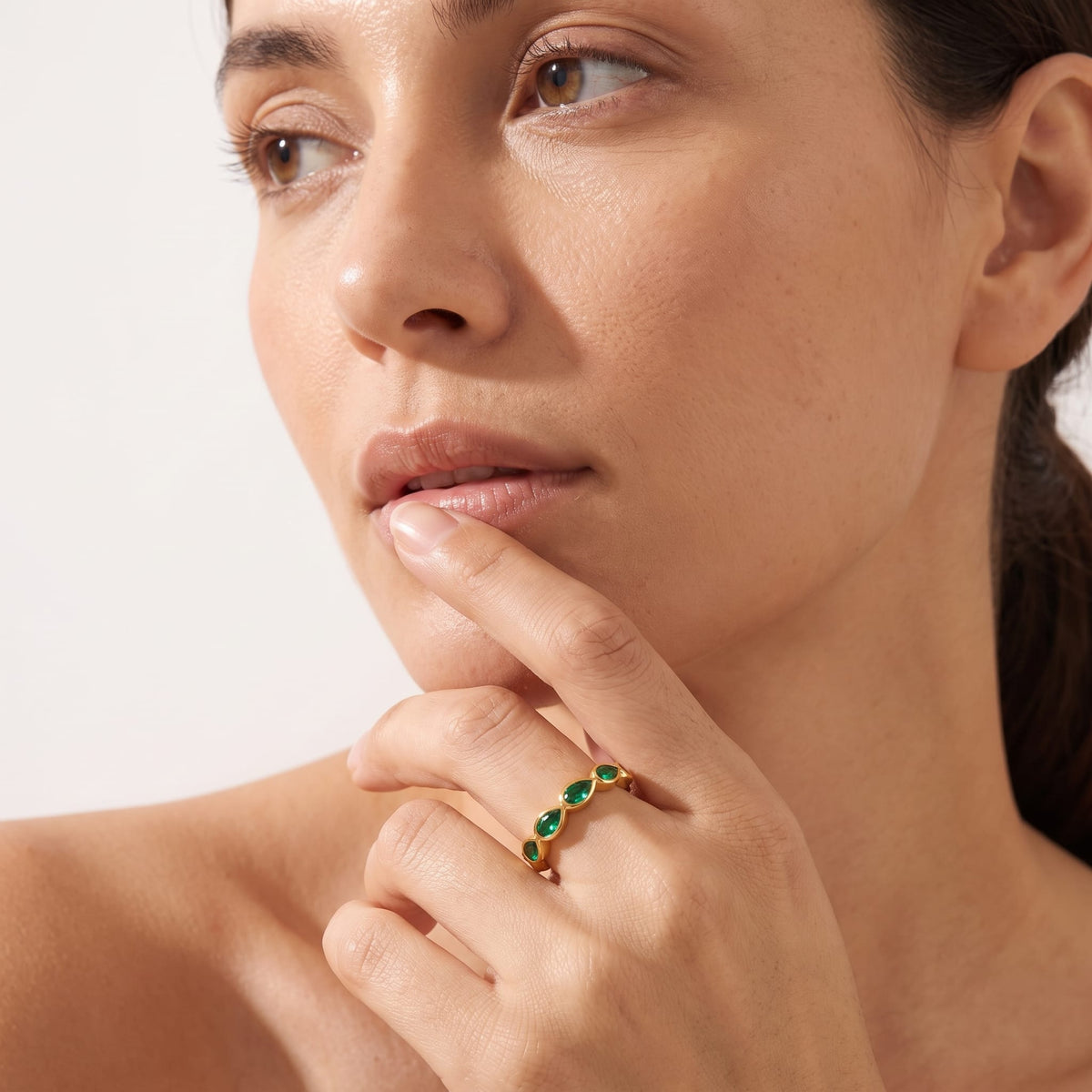 Woman wearing the Élodie green pear gold ring on the hand touching her lower lip