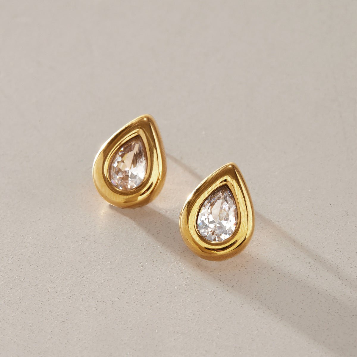 Close view of the Élodie pear-cut crystal studs in thick gold bezels on a beige surface