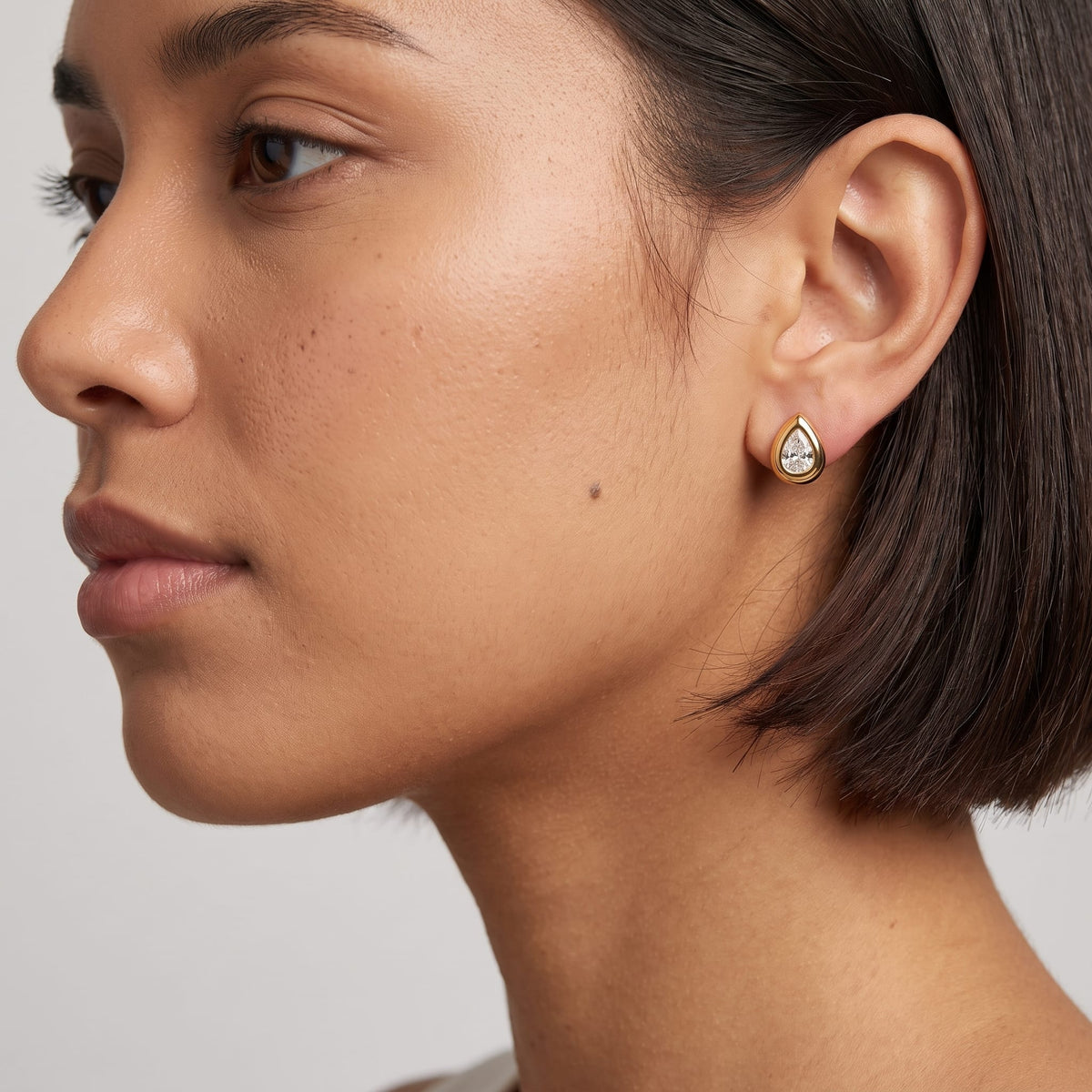 Woman wearing the Élodie teardrop bezel gold earrings on the ear with short dark hair