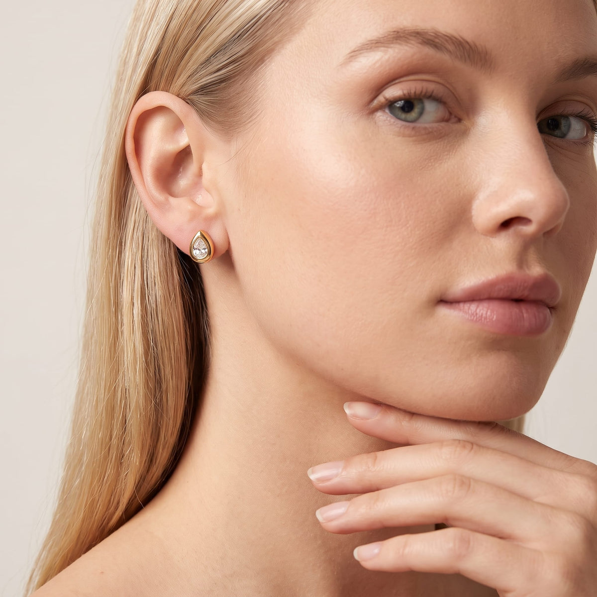 Woman wearing the Élodie teardrop bezel gold earrings on the ear while resting chin on hand