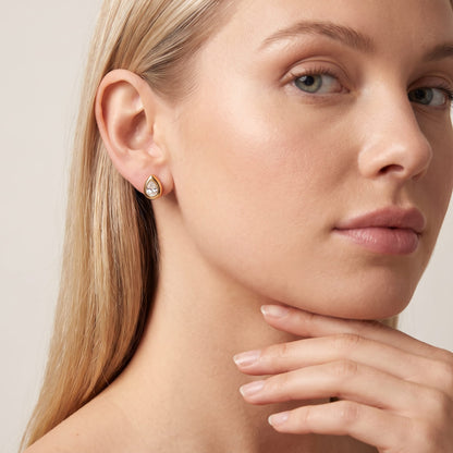 Woman wearing the Élodie teardrop bezel gold earrings on the ear while resting chin on hand