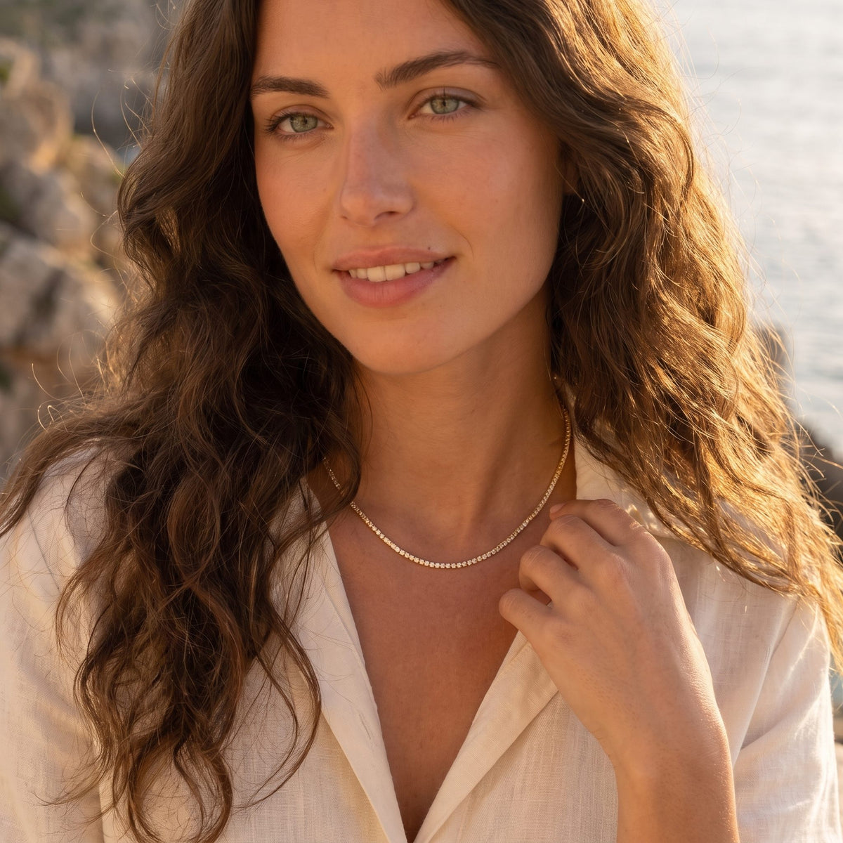 Woman by the sea at golden hour wearing the Emma tennis chain gold necklace