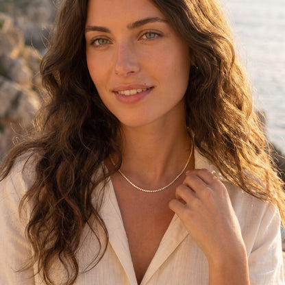 Woman by the sea at golden hour wearing the Emma tennis chain gold necklace