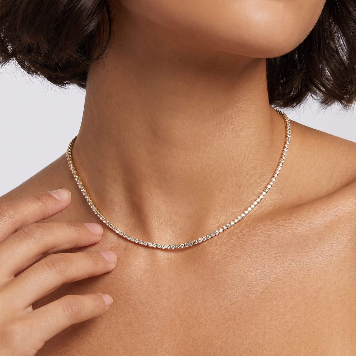 Woman with a dark bob wearing the Emma tennis chain gold necklace, one hand raised near her neck