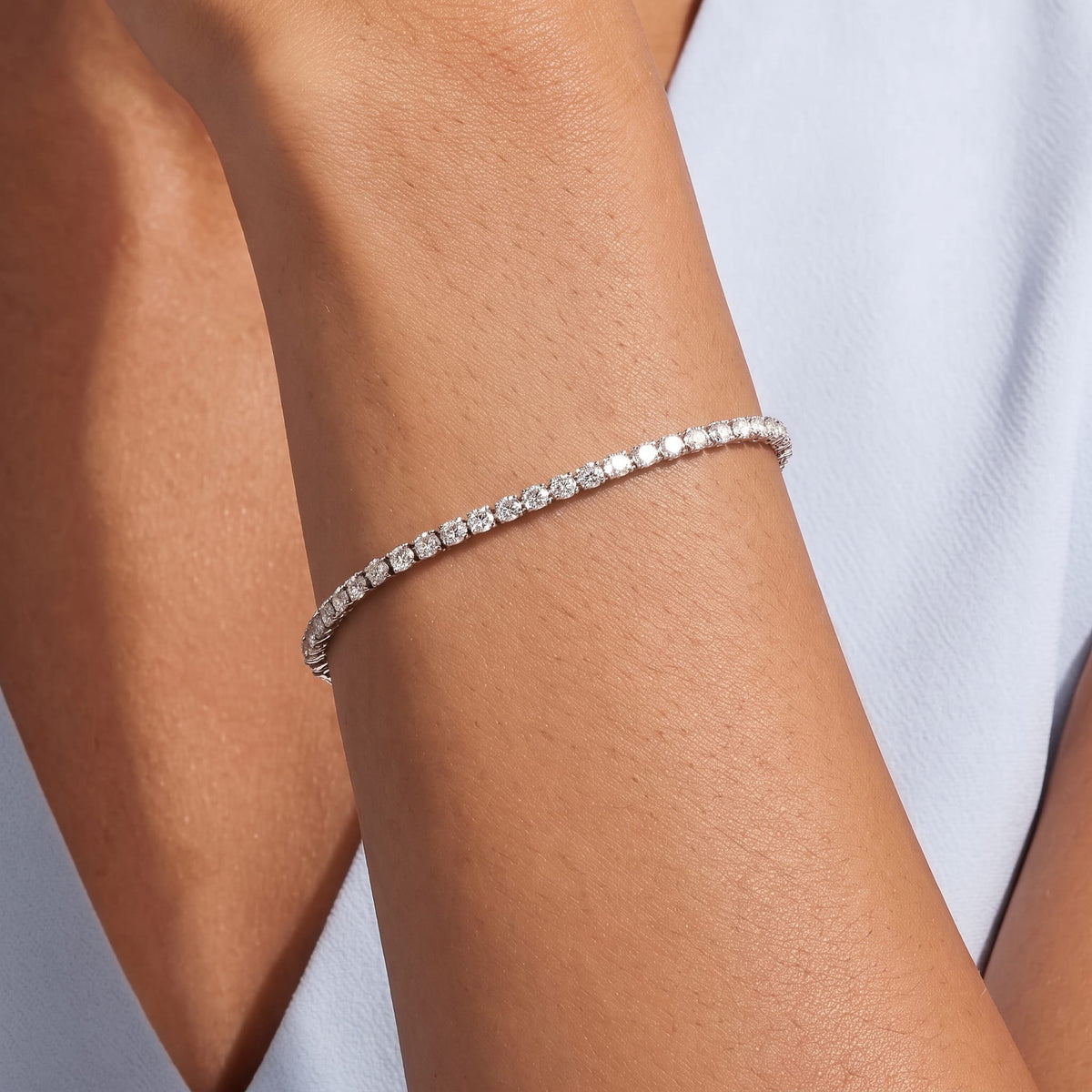 Woman in a pale blue top wearing the Emma tennis chain silver bracelet on her raised wrist