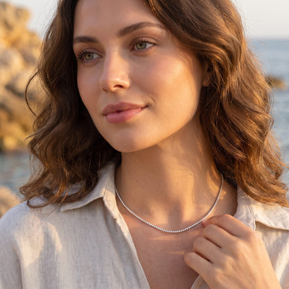 Woman by the sea at golden hour wearing the Emma tennis chain silver necklace