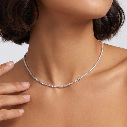 Woman with a dark bob wearing the Emma tennis chain silver necklace, one hand raised near her neck