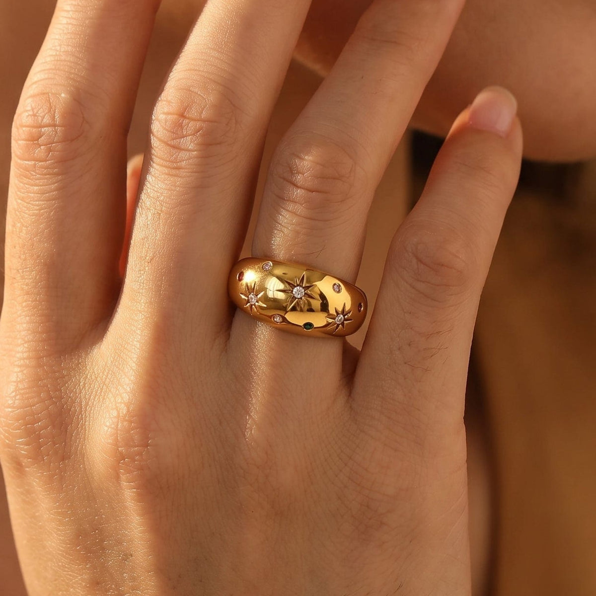 Woman wearing the Estelle star dome gold ring on the hand, resting her fingers near her face