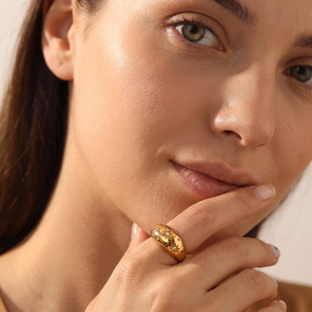 Woman wearing the Estelle star dome gold ring on the hand touching her chin in extreme close-up
