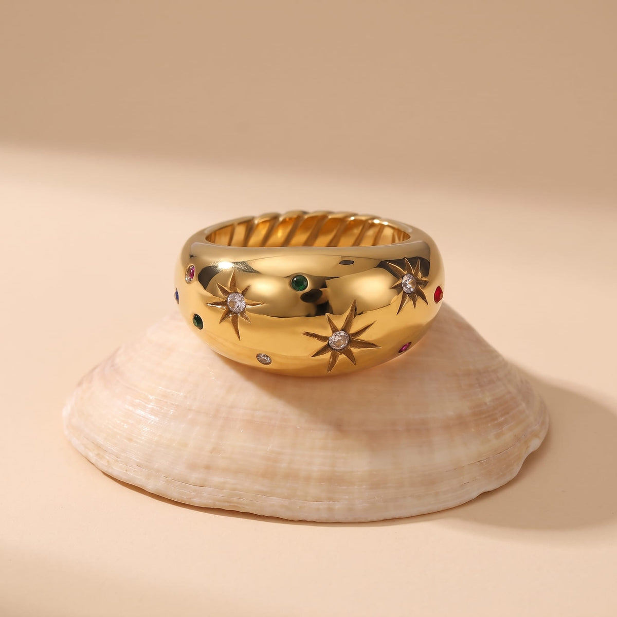 Estelle star dome gold ring on a seashell against a beige background