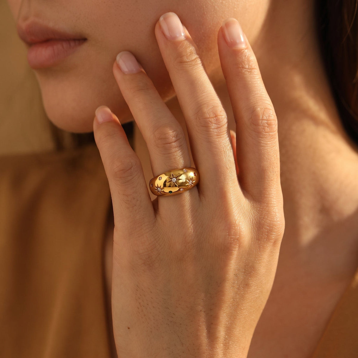 Wider view of a woman wearing the Estelle star dome gold ring on the hand, resting her fingers near her face