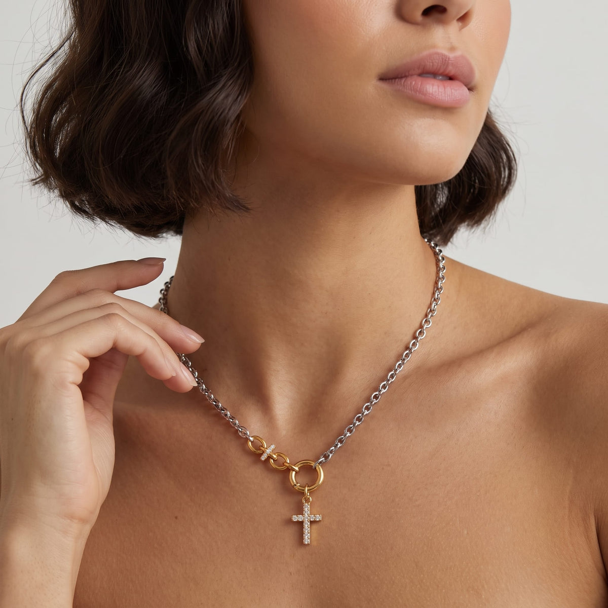 Woman wearing the Eugénie cross charm two-tone necklace at the collarbone while touching her hair
