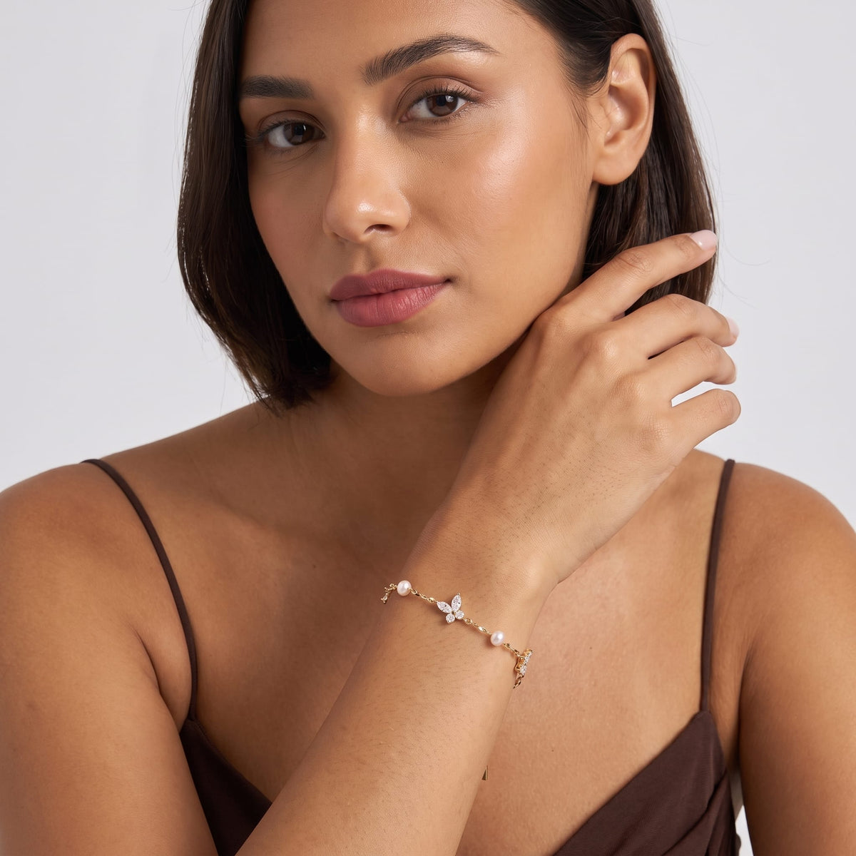 Woman wearing the Fabiola crystal butterfly gold bracelet on the wrist wearing a brown strap top