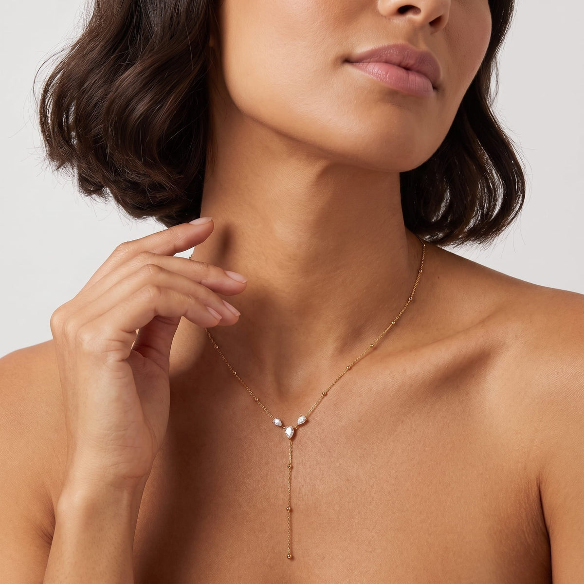 Woman wearing the Fabiola pear trio gold necklace at the collarbone with her hand raised