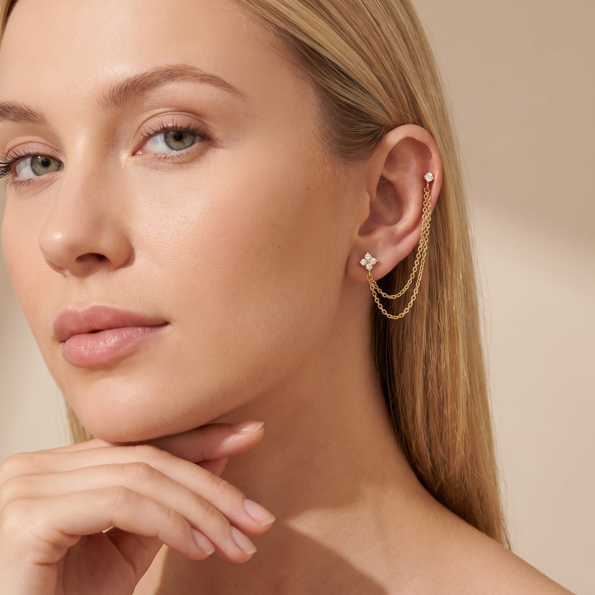 Woman wearing the Félicie flower chain gold earrings on her ear resting hand under chin