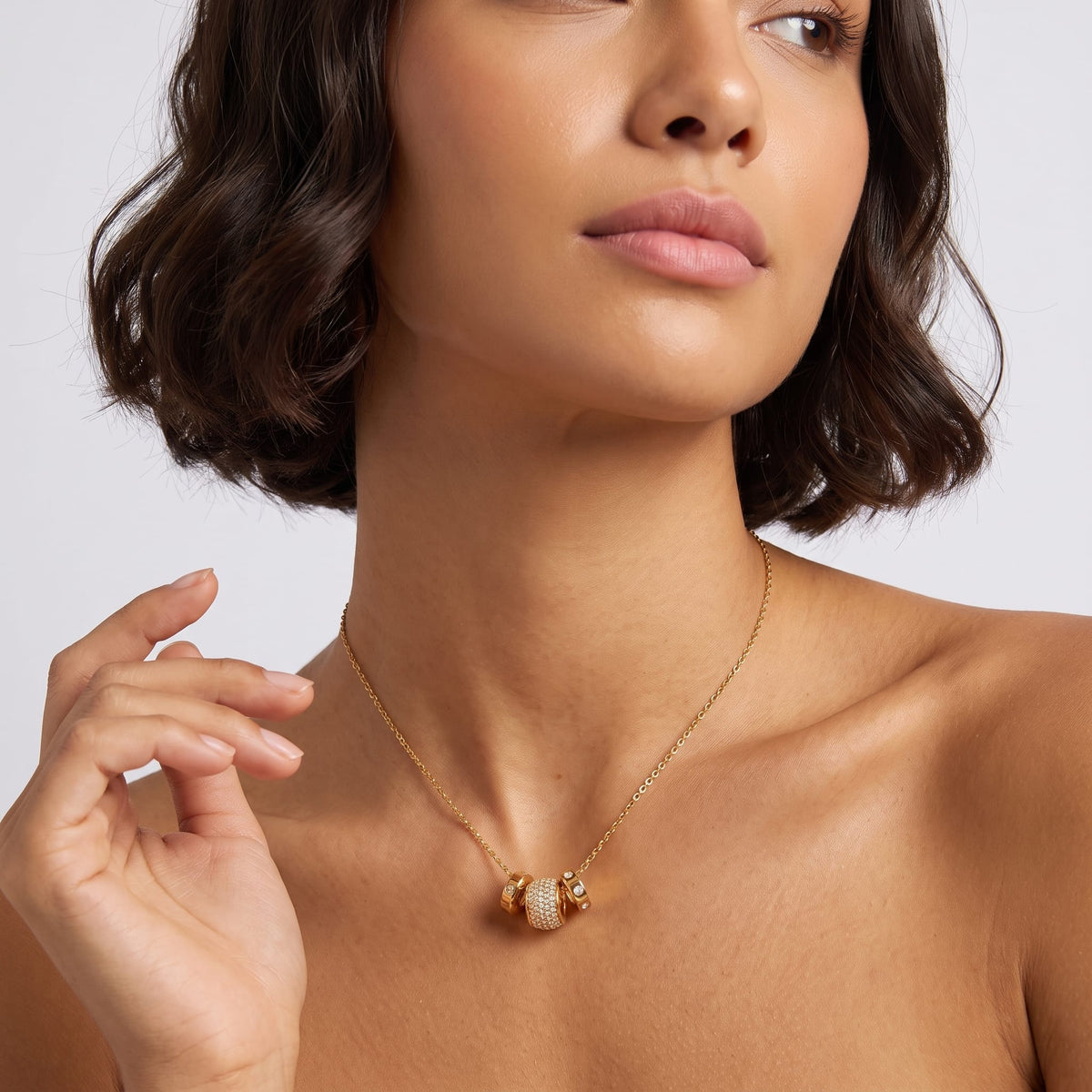 Woman wearing the Fiona pavé rondelle gold necklace at the collarbone while raising her right hand