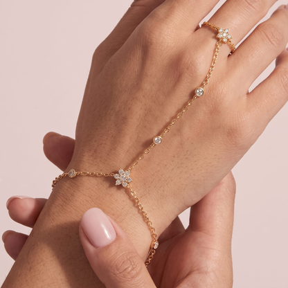 Woman wearing the Flavia gold hand chain with crystal flowers at the wrist and on a finger ring