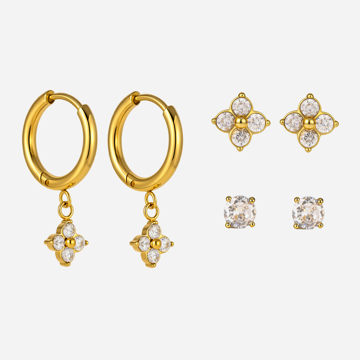 Fleur clover trio gold earrings: clover drop huggies, clover studs and round crystal studs on gray