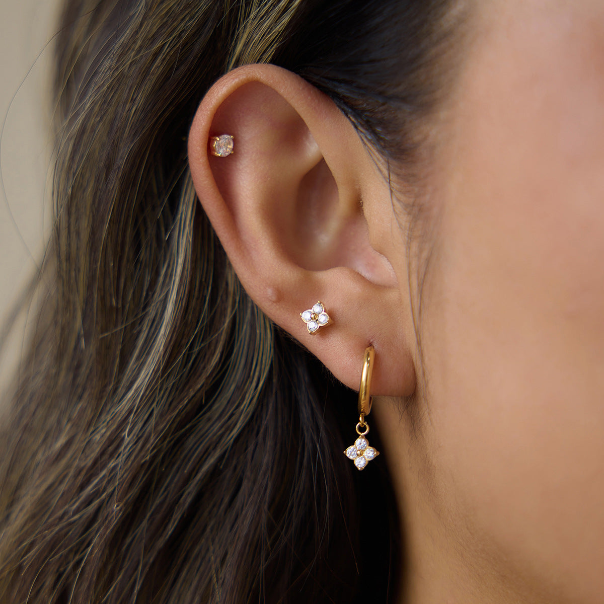 Ear wearing a Fleur round stud in the helix, a clover stud and a clover huggie in the lobe