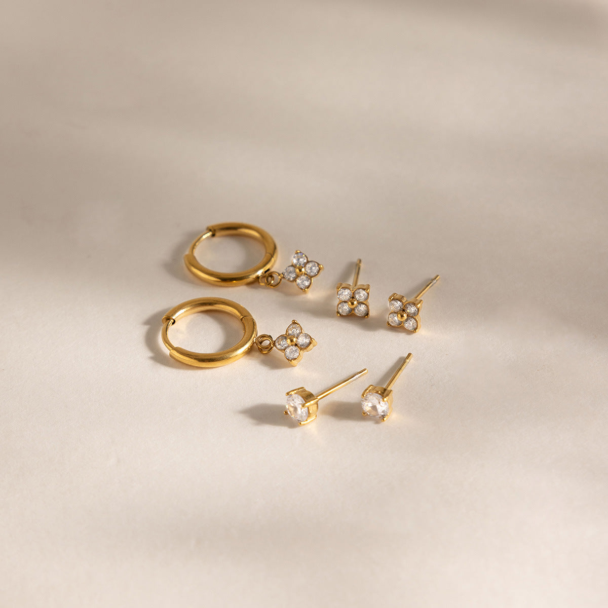 Fleur clover huggies and two pairs of crystal studs laid on a cream surface