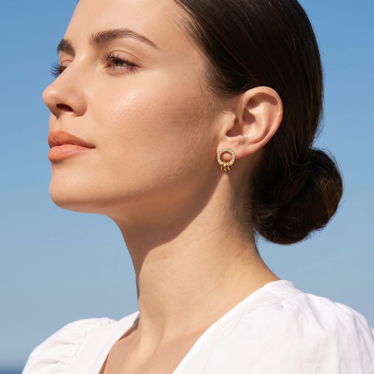 Woman wearing the Gabrielle triple ring gold earrings on the ear wearing a white top outdoors