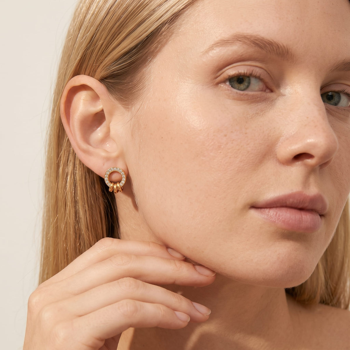 Woman wearing the Gabrielle triple ring gold earrings on the ear touching her chin with hand