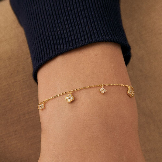 Gold anklet with floral charms on a person's ankle against a brown background