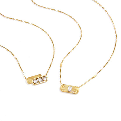 Ginevra triple heart pendant beside an emerald-cut sunburst tag necklace on white