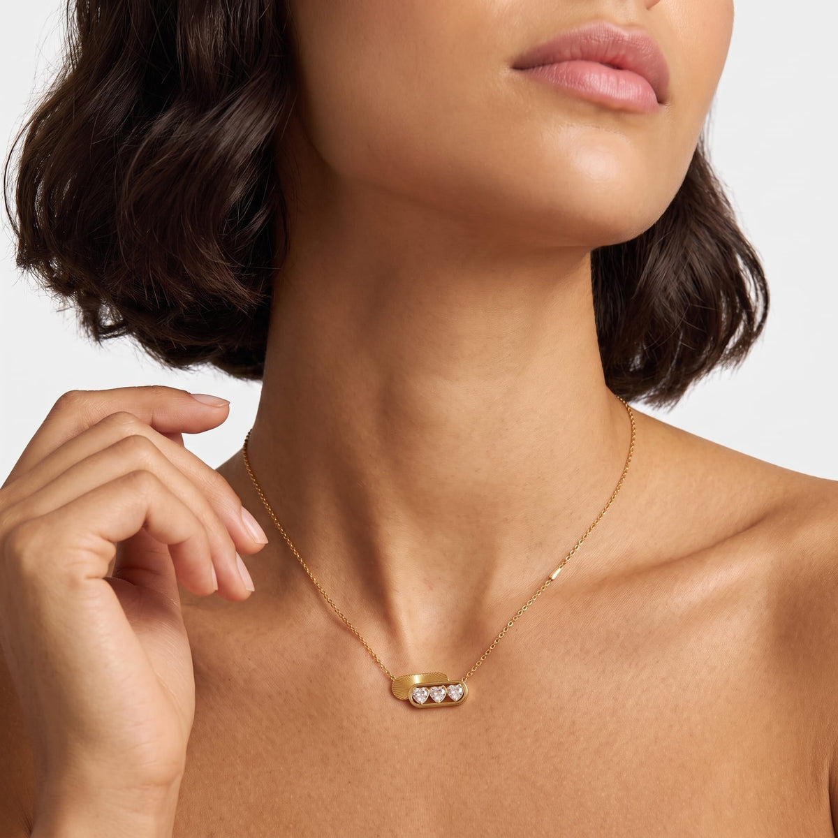 Woman wearing the Ginevra triple heart gold necklace at the collarbone touching her hair