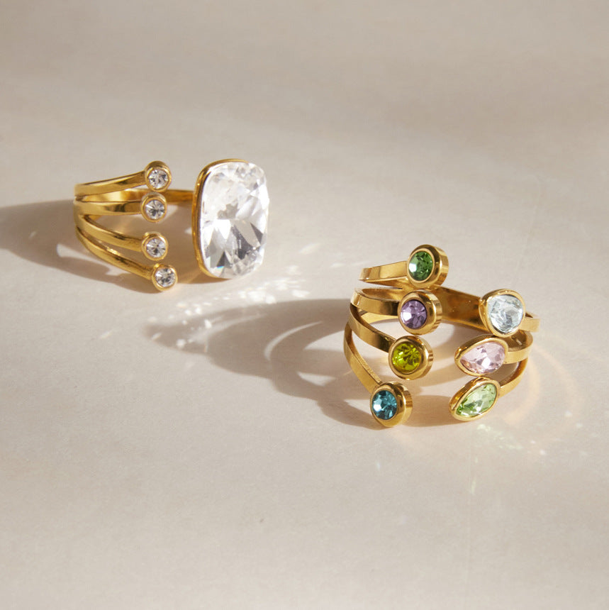 Giulia pastel crystal gold ring beside the Olivia cushion crystal ring on a cream surface