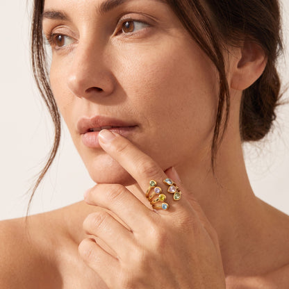 Close-up of a woman's face and hand wearing the Giulia pastel crystal gold ring