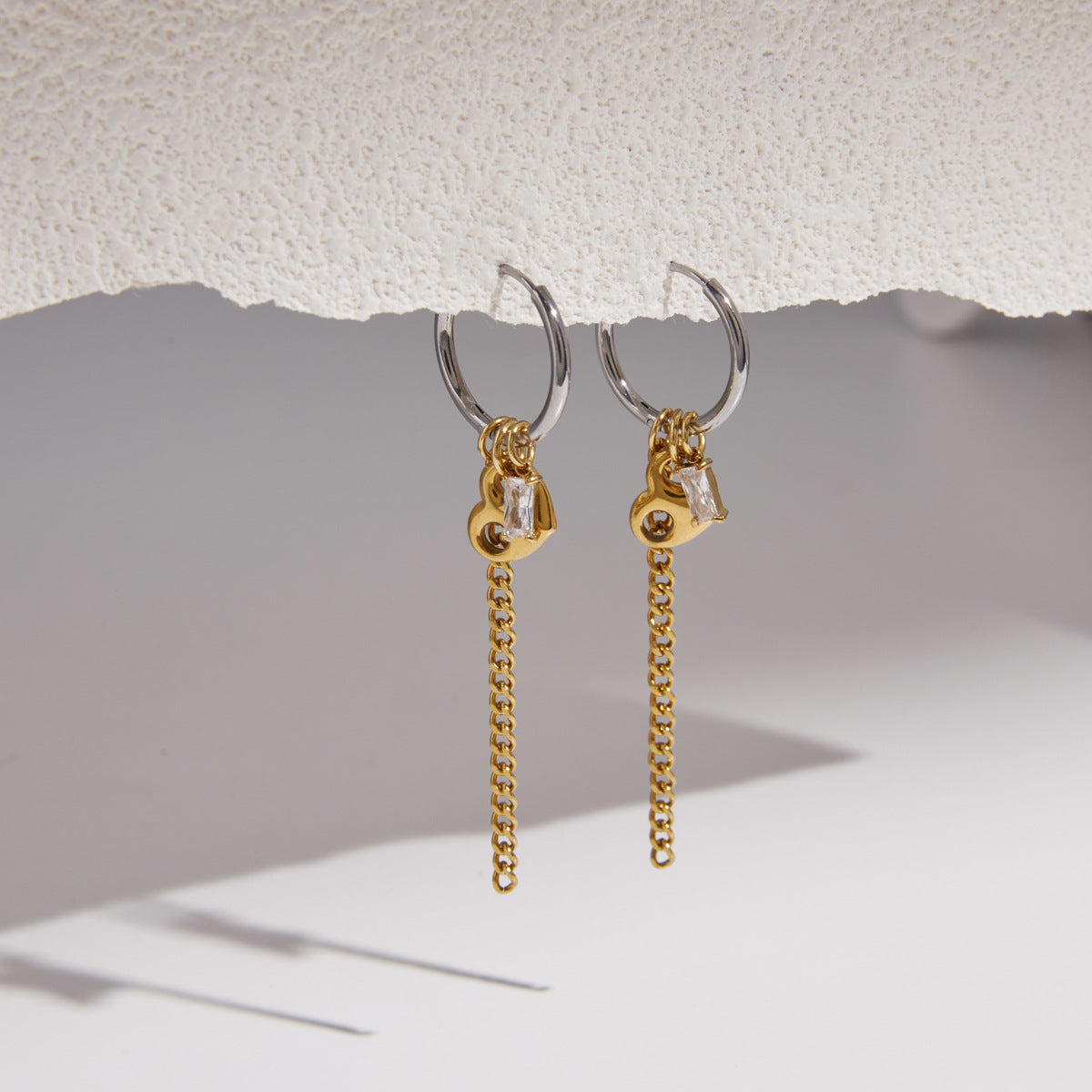 Pair of Greta two-tone earrings hanging from a textured white ledge with soft shadows below