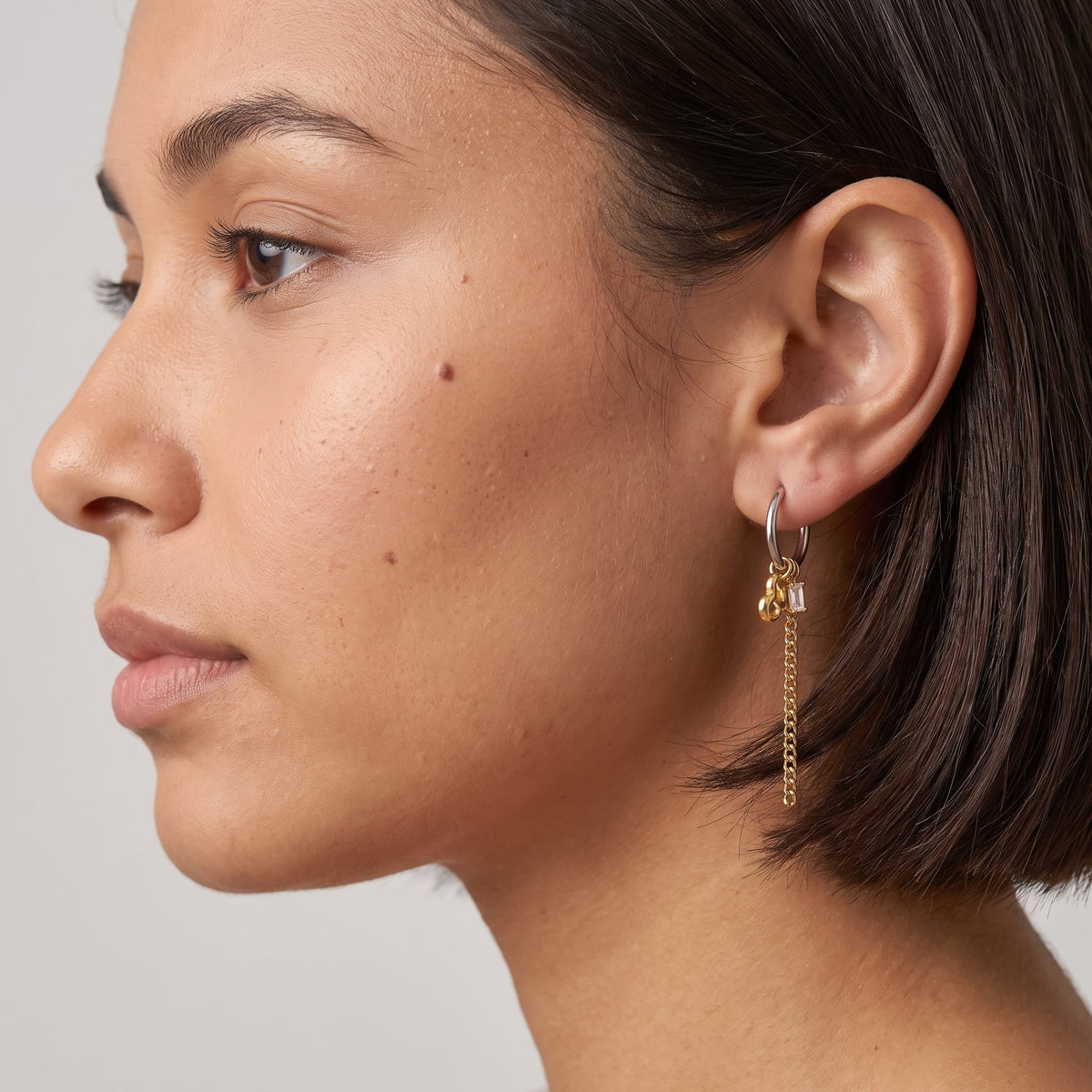 Woman wearing the Greta heart chain two-tone earrings on the ear with short dark hair profile