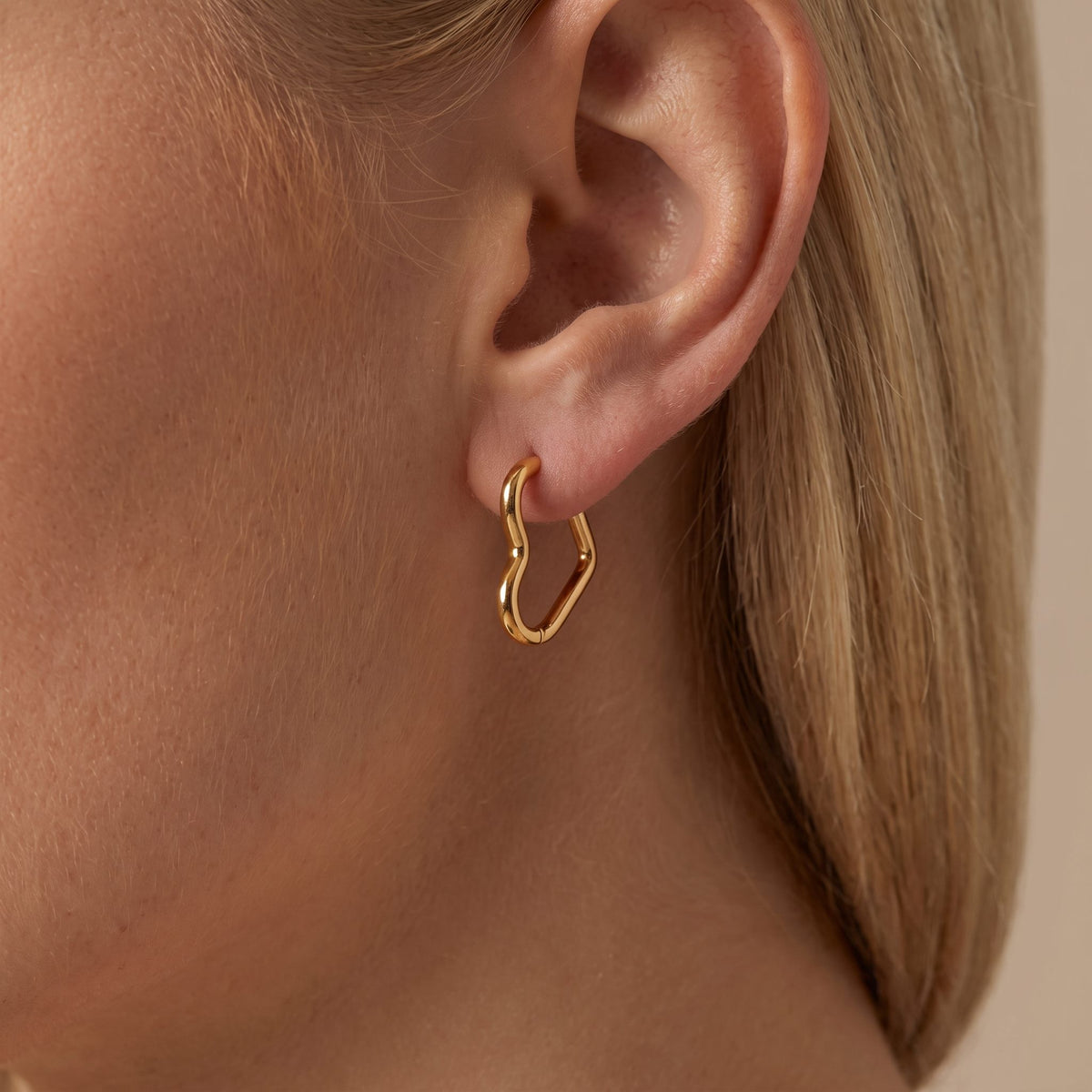 Woman wearing the Helena slim gold heart-shaped wire hoop on the earlobe