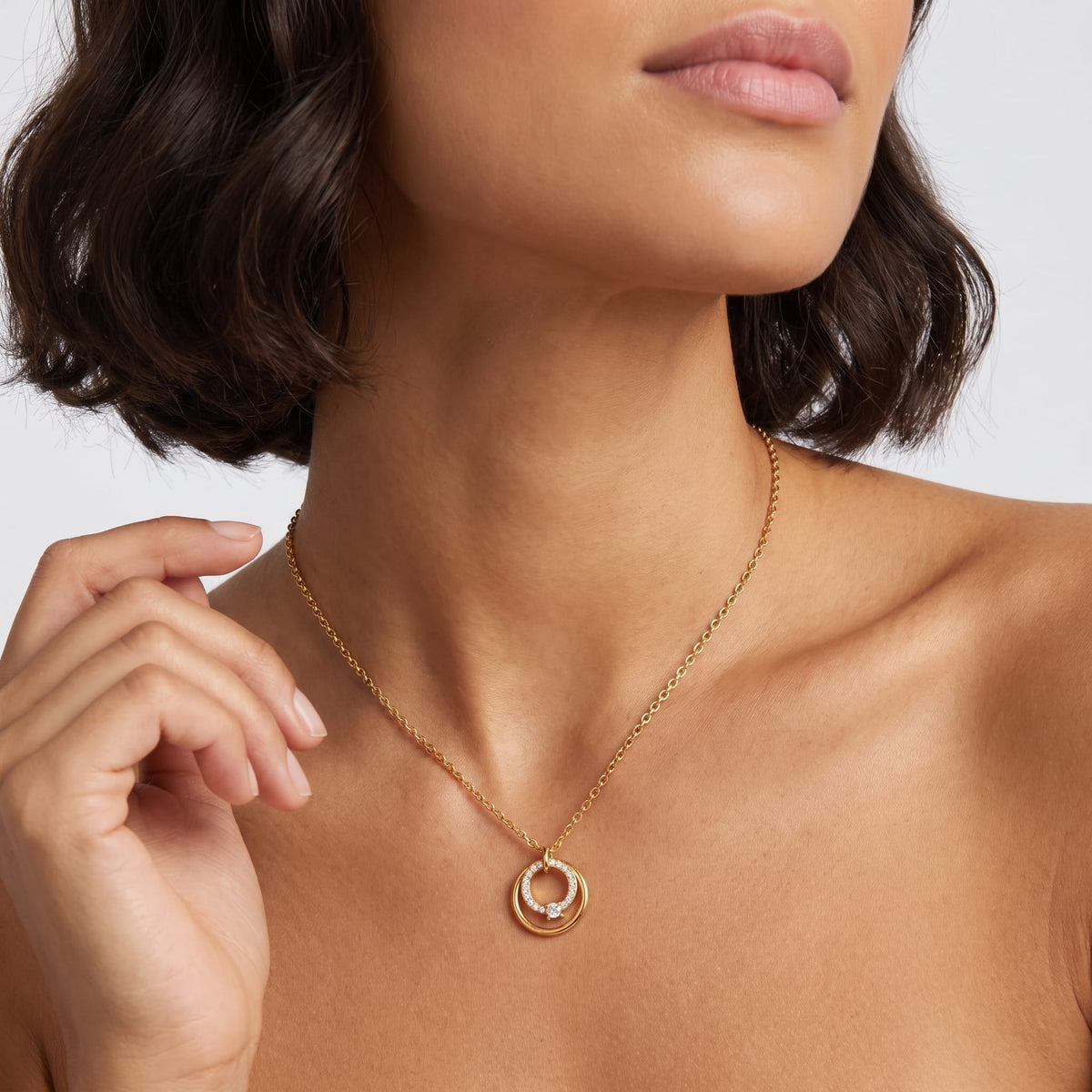Woman wearing the Héloïse double circle gold necklace at the collarbone raising one hand near neck