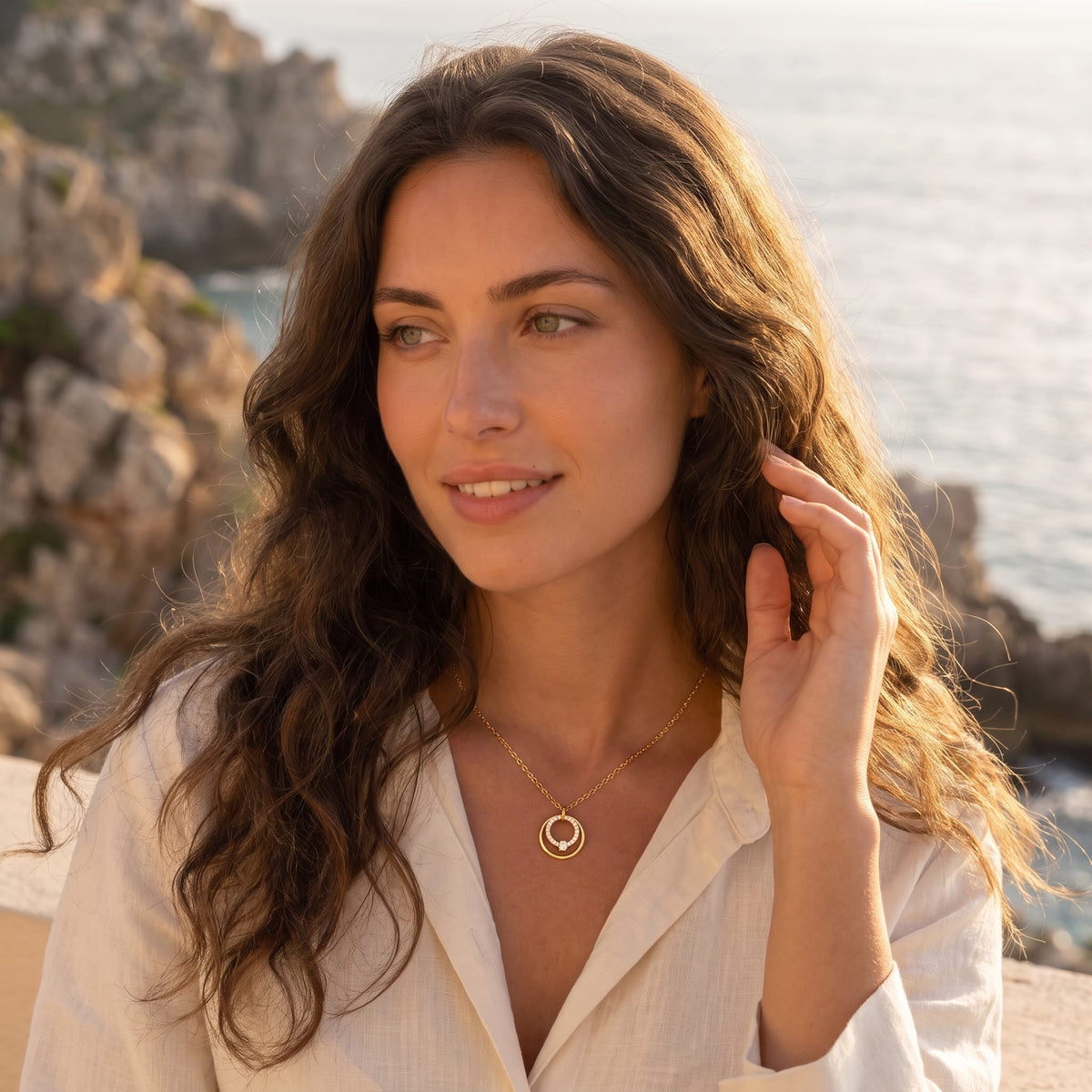 Woman wearing the Héloïse double circle gold necklace at the collarbone in a white linen shirt outdoors