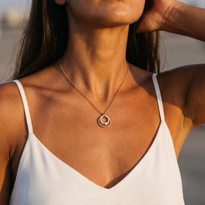 Woman wearing the Héloïse double circle gold necklace at the collarbone in a white strap top