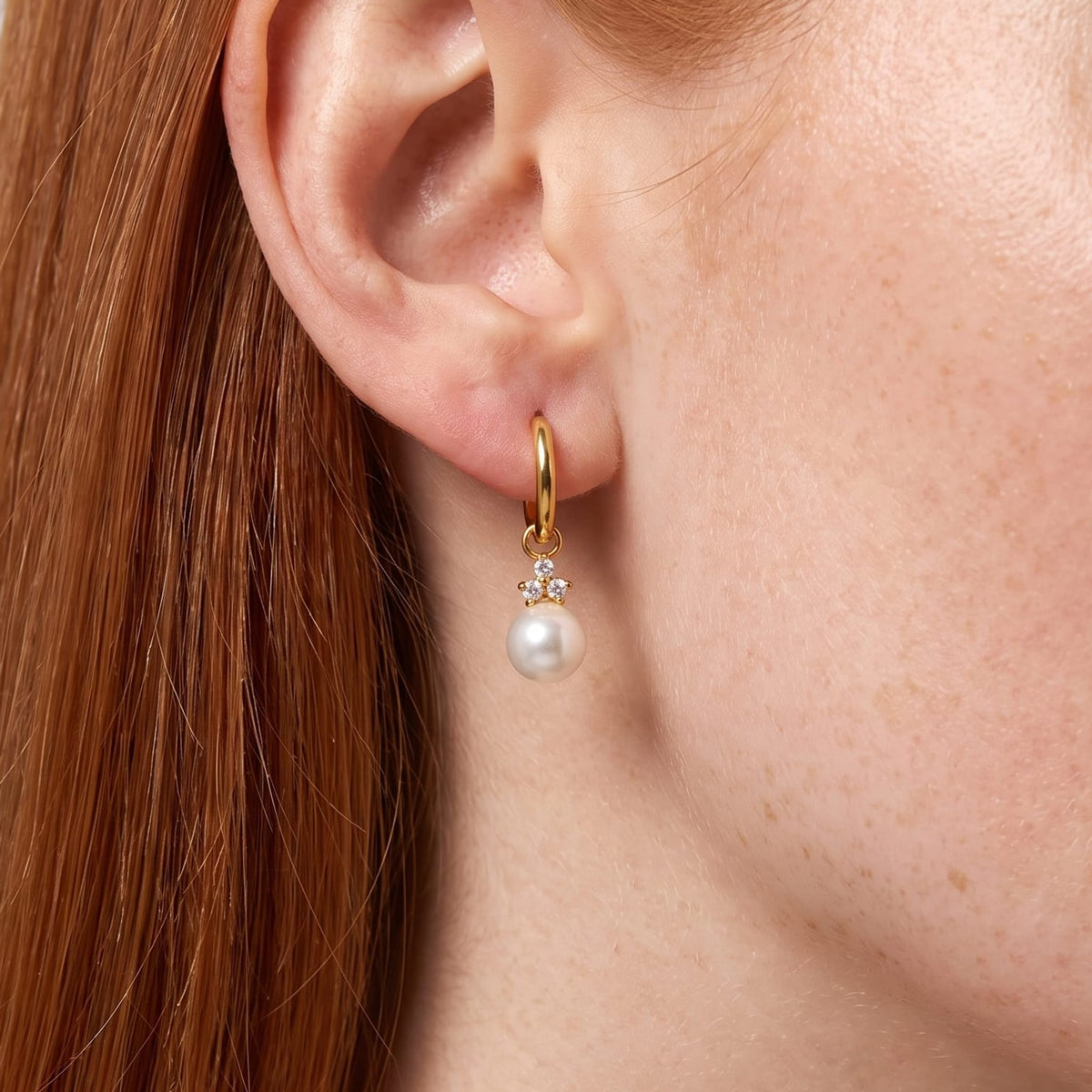 Woman wearing the Hortense pearl huggie gold earrings on her ear in a close up shot