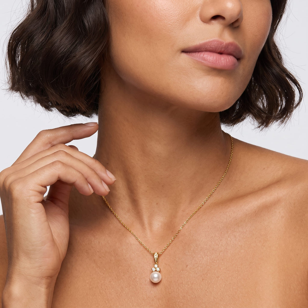 Woman wearing the Hortense pearl pendant gold necklace at the collarbone while touching her hair