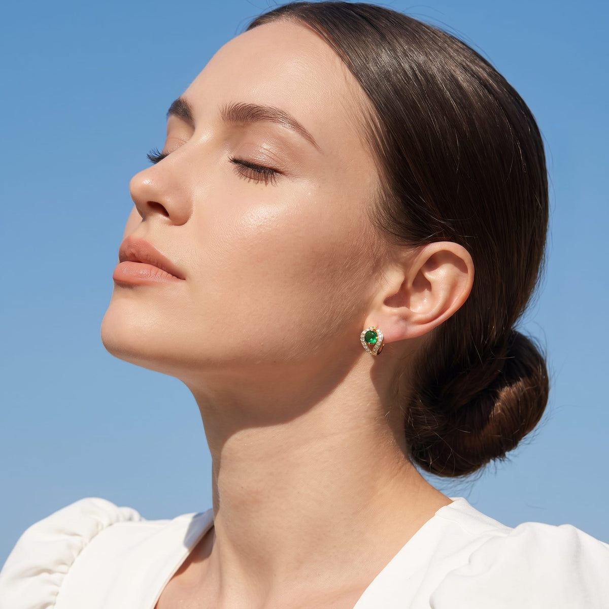 Woman wearing the Ilaria green halo gold earrings on the ear against a clear blue sky