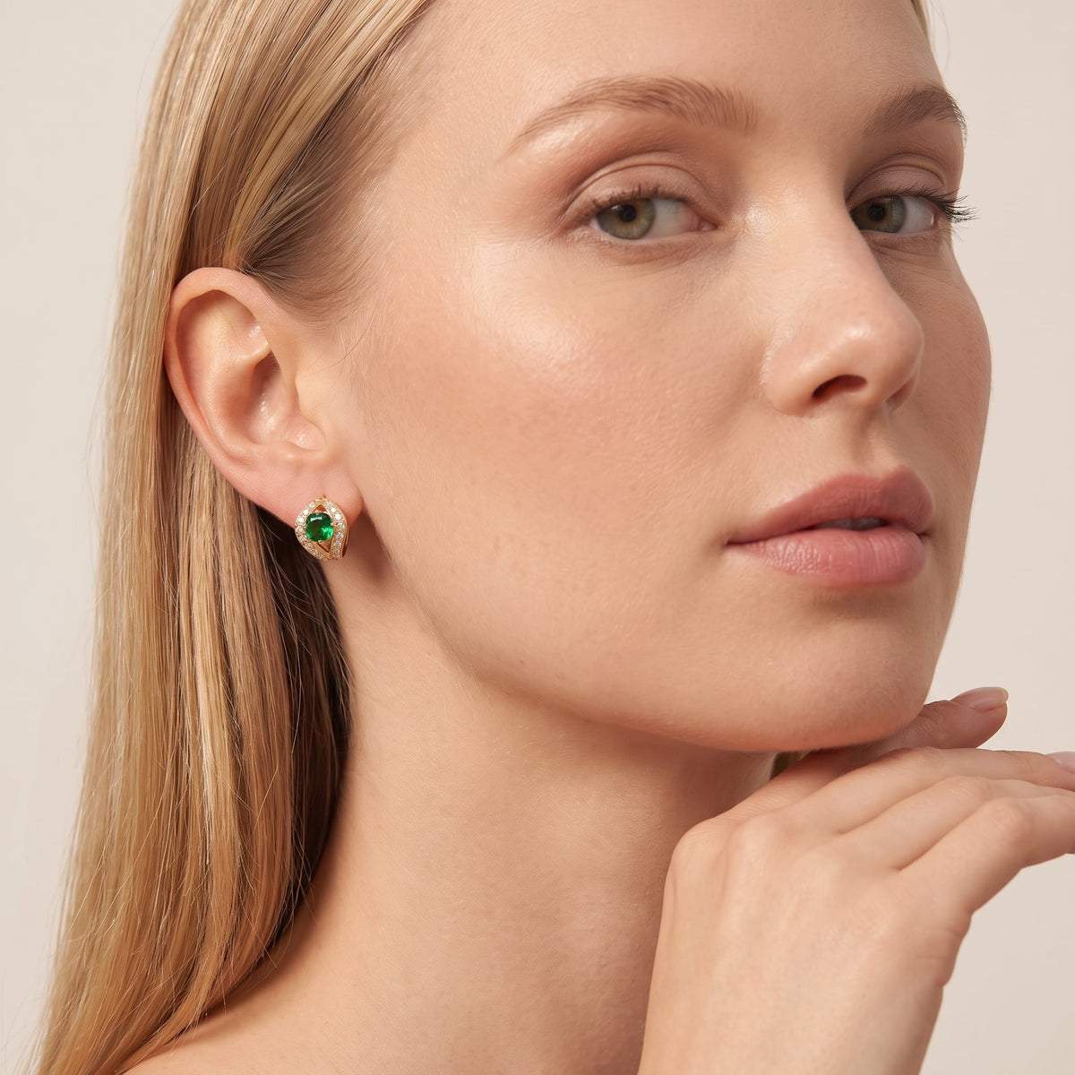 Woman wearing the Ilaria green halo gold earrings on the ear resting her hand under chin