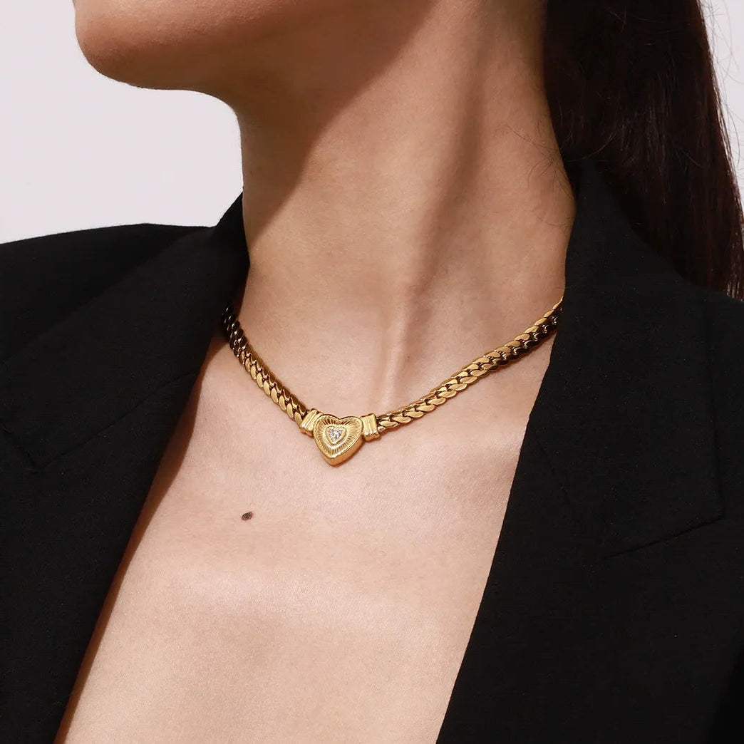 Gold chain necklace with a heart pendant worn by a person against a neutral background