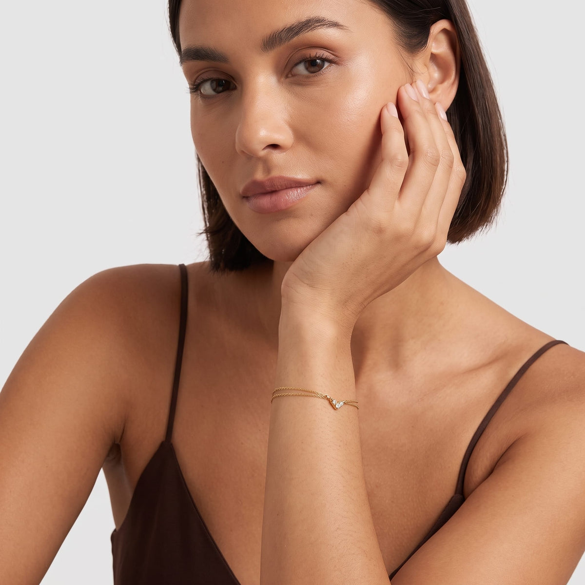 Woman wearing the Inès crystal chevron gold bracelet on the wrist while leaning her hand on her jaw