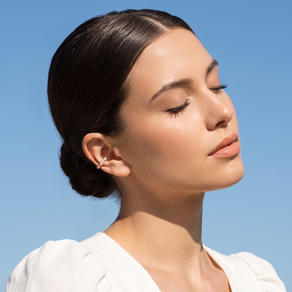 Woman wearing the Irène marquise gold ear cuffs on the ear against a blue sky background