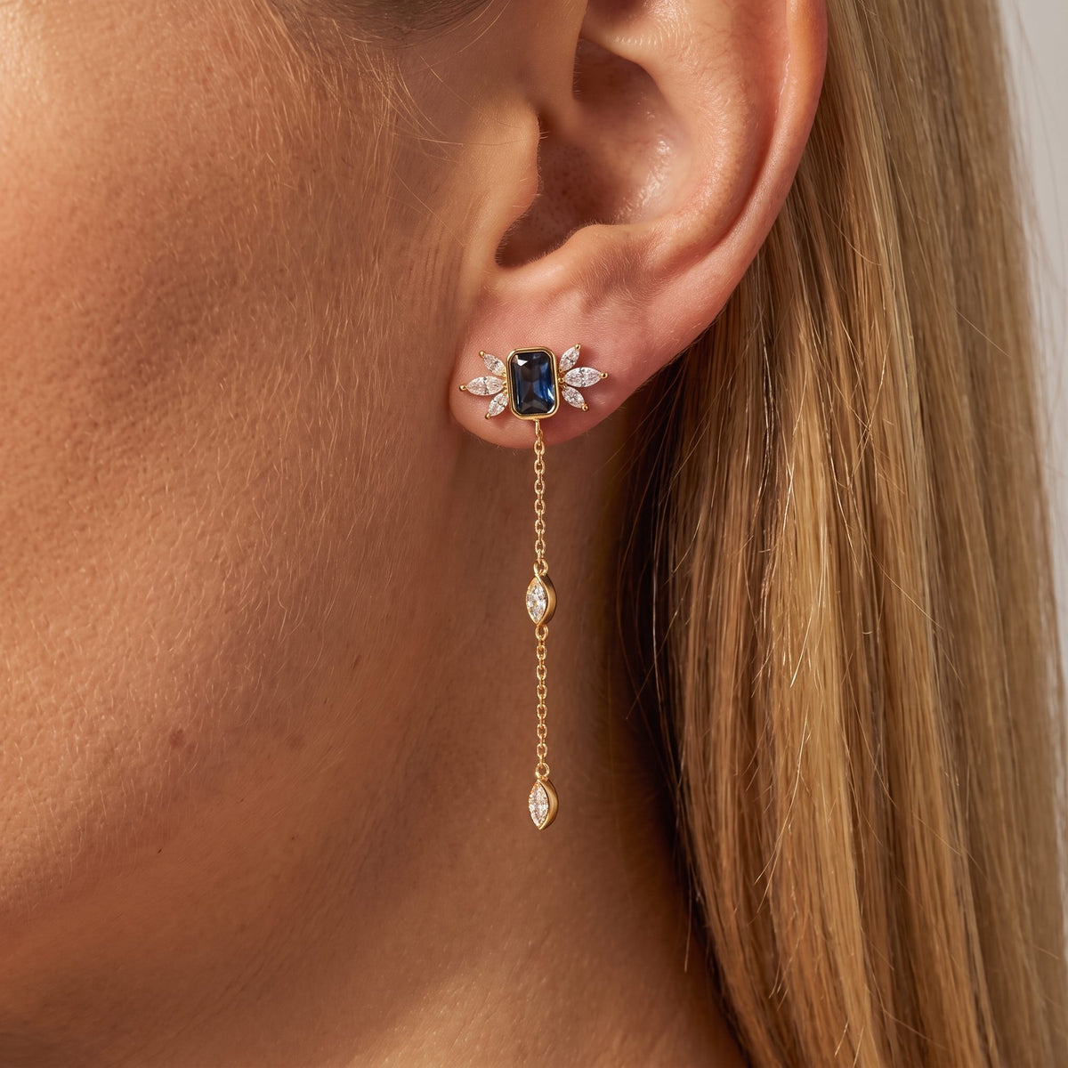 Woman wearing an Isabella Noir gold earring with a deep blue stone, crystal leaves and a chain drop