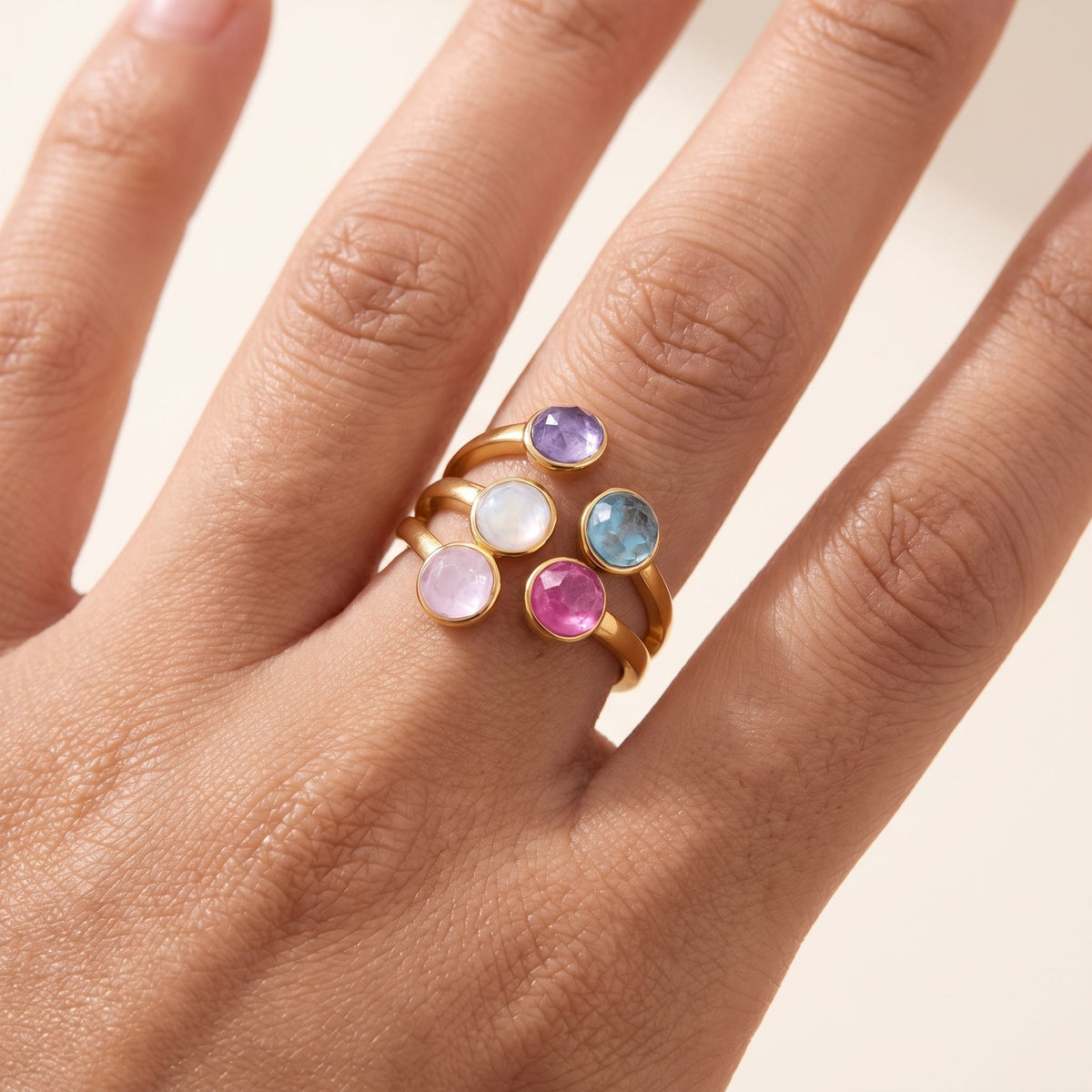 Close-up of the Isabella rainbow stone gold ring worn on a ring finger