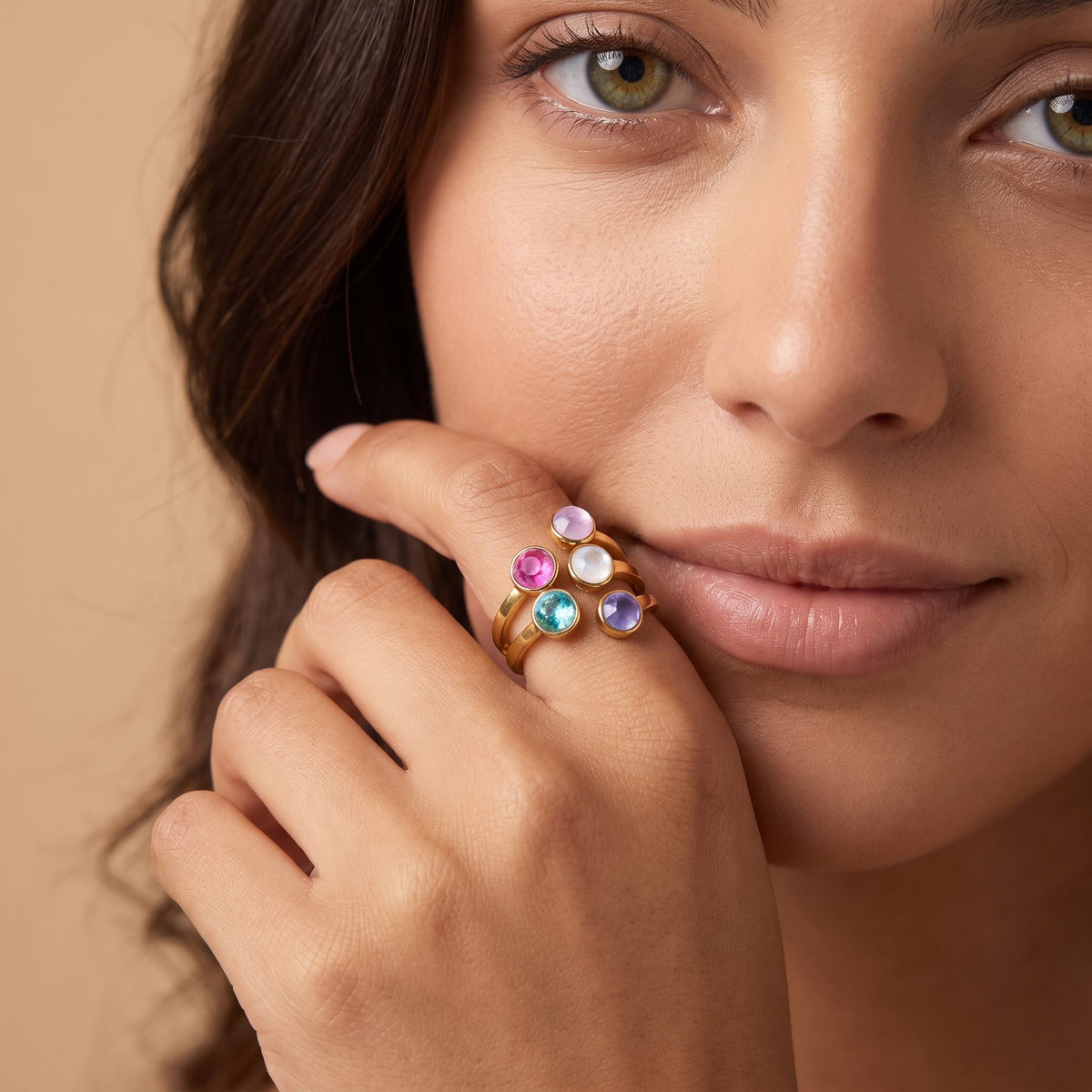 Woman with a fingertip at her lip, wearing the Isabella rainbow stone gold ring