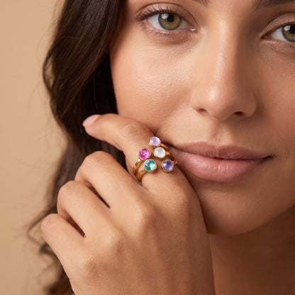 Woman with a fingertip at her lip, wearing the Isabella rainbow stone gold ring
